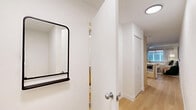 This 360 square foot studio apartment in Seattle offers a thoughtfully designed living space that maximizes functionality and style. The modern kitchen is equipped with stainless steel appliances, including a full-size refrigerator and range. Light wood cabinetry contrasts beautifully with white upper cabinets and a sleek white countertop, creating a bright and airy feel.

The bedroom area, while open to the main living space, is well-defined and features a comfortable bed, stylish floor lamp, and abstract wall art. A green accent chair adds a pop of color and provides additional seating. The bathroom boasts a clean, contemporary design with a white vanity, large mirror, and a bathtub/shower combo accented by a vibrant orange shower curtain.

Throughout the apartment, light wood flooring adds warmth and continuity. The space is illuminated by a combination of natural light from the windows and modern lighting fixtures, including a ceiling fan in the bedroom area. Despite its compact size, the apartment feels spacious and welcoming, offering a cozy urban retreat in the heart of Seattle.