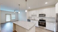 Located at 125 New Hanover St in Beaufort, SC, this thoughtfully designed one-bedroom, one-bathroom home offers a clean, modern aesthetic throughout its efficiently laid-out single floor. The kitchen serves as the centerpiece of the space, showcasing a large granite-topped island with pendant lighting overhead, crisp white shaker cabinetry, a subway tile backsplash, and a full suite of stainless steel appliances including a refrigerator, electric range, microwave, and dishwasher. Light wood-look flooring flows seamlessly throughout the home, enhancing the bright and airy atmosphere. The living area features a ceiling fan and access to natural light through a window and sliding door. The spacious bedroom includes its own ceiling fan, a well-sized window for natural light, and direct access to a walk-in closet with built-in shelving. The bathroom is finished with a granite-topped vanity, a tub-shower combination with tile surround, and accessible grab bars. Additional conveniences include a dedicated utility room and a closet for extra storage. The home presents a cohesive, contemporary design with neutral tones and quality finishes throughout.