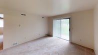 This 2-bedroom, 1-bathroom residence is laid out across a single floor, offering a functional and efficiently organized living space. The living room features neutral wall-to-wall carpeting and a full-width sliding glass door fitted with vertical blinds, providing direct outdoor access and filling the room with natural light and greenery views. Ventilation is supported by ceiling vents throughout.

The galley-style kitchen is equipped with dark walnut-toned cabinetry lining both walls, offering generous storage space above and below the counters. White appliances include a gas range with overhead ventilation hood and a full-size refrigerator. A double-basin stainless steel sink is positioned along the countertop, and tile flooring completes the practical design.

Each bedroom features soft carpeting and ample closet space, including a bifold closet door for convenient storage access. The full bathroom includes a tub/shower combination with a clean white surround, a toilet, a single vanity sink with a wall-mounted mirror, and tile flooring that coordinates with the kitchen. The overall color palette is light and neutral throughout, creating a clean and cohesive atmosphere well-suited for everyday living.