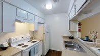 This two-floor residence offers a practical and well-organized layout designed to maximize everyday living. The kitchen is a standout functional space, designed in a classic galley style that makes efficient use of its footprint. It features white cabinetry lining both sides, providing ample storage above and below the countertops. The counters offer a speckled granite-style surface, adding a touch of character to the space. A full suite of white appliances is included, featuring an electric coil range with an overhead ventilation hood, a full-size refrigerator, and a double-basin stainless steel sink with a window positioned above for natural light. The kitchen's dark hardwood-style flooring provides a warm contrast to the bright white cabinetry and walls. Overhead lighting keeps the space well-lit and inviting. The clean, neutral color palette throughout creates a bright and airy atmosphere. Spanning two floors, the residence provides a sense of separation between living and private spaces, offering a versatile and comfortable environment suited to a variety of lifestyles.