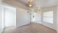 This single-floor residence offers a practical and comfortable layout designed for everyday living. The main living area is a standout feature, showcasing vaulted ceilings that lend a sense of openness and volume to the space. Two ceiling fans are installed throughout the living area, providing both function and a subtle decorative element. The floors are covered in neutral-toned carpet, which carries through the living spaces and bedrooms, creating a cohesive and warm feel underfoot. A window along one wall allows natural light to filter into the living area.

The kitchen is efficiently designed and features dark wood cabinetry, a double stainless steel sink set into a tiled countertop, and includes a dishwasher and range. A pass-through window connects the kitchen to the living area, enhancing the open flow between spaces and allowing additional light into the kitchen.

The bedrooms are well-proportioned, each equipped with ceiling fans and windows fitted with blinds that offer privacy while still admitting natural light. The rooms are finished with the same neutral carpet found throughout the home, maintaining a consistent aesthetic.

The bathroom is finished with large-format brown tile on both the floor and the tub surround, adding a grounded, earthy tone to the space. The full bath includes a soaking tub with a showerhead, toilet, and cabinetry for storage.