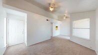 This single-floor residence offers a practical and comfortable layout designed for everyday living. The main living area is a standout feature, showcasing vaulted ceilings that lend a sense of openness and volume to the space. Two ceiling fans are installed throughout the living area, providing both function and a subtle decorative element. The floors are covered in neutral-toned carpet, which carries through the living spaces and bedrooms, creating a cohesive and warm feel underfoot. A window along one wall allows natural light to filter into the living area.

The kitchen is efficiently designed and features dark wood cabinetry, a double stainless steel sink set into a tiled countertop, and includes a dishwasher and range. A pass-through window connects the kitchen to the living area, enhancing the open flow between spaces and allowing additional light into the kitchen.

The bedrooms are well-proportioned, each equipped with ceiling fans and windows fitted with blinds that offer privacy while still admitting natural light. The rooms are finished with the same neutral carpet found throughout the home, maintaining a consistent aesthetic.

The bathroom is finished with large-format brown tile on both the floor and the tub surround, adding a grounded, earthy tone to the space. The full bath includes a soaking tub with a showerhead, toilet, and cabinetry for storage.