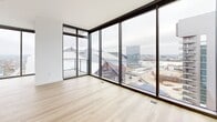 Located in the heart of Atlanta, this contemporary high-rise residence offers three bedrooms, three bathrooms, and two balconies across a well-appointed single floor. The open-concept kitchen and living area serves as the centerpiece of the home, featuring sleek flat-front cabinetry in warm gray tones, quartz countertops, a large island with an undermount sink and matte black fixtures, and stainless steel appliances with a subway tile backsplash. Floor-to-ceiling windows flood the living space with natural light and frame sweeping panoramic views of the Atlanta skyline, including prominent landmarks visible from high above the city. Light hardwood flooring flows throughout, complementing the crisp white walls and modern aesthetic. The primary bedroom is generously sized with direct access to a private balcony and floor-to-ceiling glazing. Its en-suite bathroom features a double-sink floating vanity with quartz countertops, matte black hardware, large-format tile flooring, and a glass-enclosed shower. Secondary bedrooms are bright and well-proportioned, each with closet storage and easy bathroom access. Additional highlights include a dedicated laundry area, utility room, and ample closet space throughout, making this a highly functional and stylish urban residence.