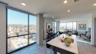 Located at 111 E Central Pkwy in Cincinnati, Ohio, this high-rise residence delivers a contemporary urban living experience defined by expansive floor-to-ceiling windows that frame panoramic views of the Cincinnati skyline and surrounding hillsides. The open-concept living and dining area is anchored by corner window walls, flooding the space with natural light and showcasing exposed concrete structural columns that lend an industrial-modern character to the interior.

The kitchen is well-appointed with dark wood cabinetry extending to the ceiling, stainless steel appliances including a range, microwave, and refrigerator, white subway tile backsplash, and a generous island with a white quartz countertop and bar seating. The dining area, positioned alongside floor-to-ceiling windows, offers an elevated cityscape backdrop.

The bedrooms are comfortably scaled, with one featuring a large window overlooking downtown Cincinnati, and another served by a spacious walk-in closet with built-in shelving and hanging storage. The primary bathroom includes a dual-sink vanity with ample cabinetry, a glass-enclosed subway tile shower, and recessed lighting. A secondary bathroom features a subway tile tub-shower combination. Recessed lighting and ceiling fans are present throughout the residence.