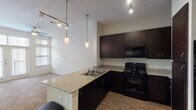 This 1-bedroom, 1-bathroom unit in Houston, TX (77025) is a single-story residence thoughtfully designed for comfortable urban living. The open-concept kitchen serves as the centerpiece of the living area, outfitted with rich dark-espresso cabinetry, granite countertops, and a full suite of black appliances including a range, microwave, dishwasher, and refrigerator with an ice and water dispenser. A peninsula with an integrated sink extends the counter space and creates a natural divide between the kitchen and living area, while pendant lighting and track lighting illuminate the space stylishly. Wood-style flooring runs throughout the kitchen and entryway, adding warmth and easy maintenance. The bedroom is carpeted and benefits from large windows that allow natural light to filter in. The bathroom is well-appointed with tile flooring, a soaking tub with tiled surround, a dark-cabinetry vanity with a granite countertop, and direct access to a walk-in closet complete with built-in shelving. The overall design palette is neutral and cohesive, combining clean white walls with dark fixtures and granite surfaces for a modern, polished aesthetic throughout.