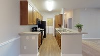 Located at 561 Hinson Dr in Myrtle Beach, SC, this single-floor unit offers a practical and comfortable layout designed for everyday living. The galley-style kitchen is well-appointed with warm honey-toned cabinetry, light granite-style countertops, and black appliances including a refrigerator, electric range, and dishwasher. Wood-look plank flooring runs the length of the kitchen, and a dedicated laundry closet at the rear of the kitchen houses a full-size washer and dryer, adding notable convenience.

The open living and dining area transitions from wood-look flooring near the entryway to plush neutral carpeting, creating distinct zones within a cohesive space. Track lighting near the entry and a front closet provide functional touches throughout. The living area extends into a sunlit area framed by multi-pane windows fitted with blinds, allowing for ample natural light.

The bedroom is generously sized, featuring soft carpeting, a ceiling fan, and access to a walk-in closet. The bathroom includes tile flooring, a single-sink vanity with wood cabinetry, a large mirror, and a tub-shower combination. Neutral gray walls throughout the unit contribute to a calm, understated ambiance.