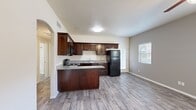 This single-story, 2-bedroom, 1-bathroom residence offers a practical and well-organized layout across its efficiently designed floor plan. The kitchen serves as a central highlight, featuring rich dark-wood cabinetry with ample upper and lower storage, granite-style countertops, a peninsula that provides additional prep space, and black appliances including a refrigerator, range, and microwave. Wood-look tile flooring runs throughout the kitchen and main living area, lending a clean and cohesive aesthetic. Natural light filters in through windows fitted with horizontal blinds, brightening the open living space adjacent to the kitchen. A distinctive arched doorway connects the kitchen area to the hallway, adding an architectural detail that enhances the overall character of the home. Both bedrooms are carpeted and offer a neutral palette with window views to the outside. The primary bedroom includes a walk-in closet with wrap-around shelving and hanging rods, providing generous storage. The full bathroom is outfitted with a tub-shower combo featuring tile surround, a vanity with dark cabinetry, and built-in open shelving for added convenience. Three closets total throughout the home ensure abundant storage capacity for everyday living.