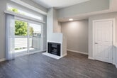 Located at 2111 W 17th St in Santa Ana, California, this single-floor unit offers a thoughtfully updated interior with a clean, contemporary aesthetic throughout. The kitchen is a standout feature, showcasing high-gloss white upper cabinetry, contrasting dark lower cabinets, crisp white quartz countertops, and stainless steel appliances including a range and over-the-range microwave. A peninsula with an integrated sink and brushed nickel faucet opens to the living area, creating a seamless flow between the cooking and gathering spaces. The living room is bright and welcoming, with wood-look plank flooring that extends throughout the unit, neutral gray-toned walls, and a white-framed fireplace that serves as a focal point. Sliding glass doors lead to a private balcony, allowing natural light to fill the space and offering outdoor views of surrounding greenery. A transom window above the doors further enhances the sense of openness. The bathroom is clean and functional, featuring a full soaking tub and shower combination with gold-tone fixtures, wood-look flooring, and a textured ceiling. The overall ambiance of the space is modern and move-in ready, with consistent finishes that lend a cohesive and polished feel throughout.