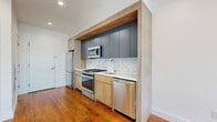 Located at 100 Tuers in Jersey City, NJ, this thoughtfully designed one-bedroom, one-bathroom unit offers a contemporary living experience with high-quality finishes throughout. The open layout maximizes the available space, with rich hardwood floors running continuously through the main living areas and bedroom, lending warmth and cohesion to the interior.

The kitchen is a standout feature, showcasing a modern design with a combination of slate-blue upper cabinetry and natural wood lower cabinets, complemented by a striking marble-look backsplash and sleek white countertops. Stainless steel appliances — including a gas range, microwave, dishwasher, and refrigerator — complete this well-appointed culinary space. A stacked in-unit washer and dryer adds everyday convenience.

The bedroom is bright and airy, benefiting from two windows that invite natural light and offer views of the surrounding neighborhood. Clean white walls and recessed lighting create a calm, neutral atmosphere throughout.

The bathroom features wood-look tile wall accents, a natural wood vanity with a white countertop, terrazzo-style flooring, and a full soaking tub, combining contemporary design with functional comfort. The overall ambiance of the unit is clean, modern, and move-in ready, making it an excellent choice in the heart of Jersey City.