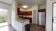 This single-floor residence offers a thoughtfully designed layout that balances comfort and functionality. The open-concept kitchen is a standout feature, equipped with rich cherry wood cabinetry, granite-style countertops, a classic subway tile backsplash, and a full suite of stainless steel appliances including a refrigerator, electric range with over-the-range microwave, and dishwasher. A peninsula with a built-in sink provides additional workspace and casual seating, seamlessly connecting the kitchen to the living area.

The living space is bright and open, featuring dark hardwood-style flooring that transitions into plush carpeting. A ceiling fan with light fixture adds both comfort and character, while a graceful arched doorway leads toward the bedroom corridor. Sliding glass doors open to a private balcony, inviting natural light and outdoor views into the home.

The bedrooms are generously sized, each finished with soft carpeting and windows that provide natural light. One bedroom includes a ceiling fan and walk-in closet access. The primary bathroom features a dual-sink vanity with dark stone countertops, rich wood cabinetry, a tiled shower, and hardwood-style flooring. A secondary bathroom offers a single-sink vanity with matching cabinetry and stone countertop, maintaining a consistent and cohesive design aesthetic throughout the home.