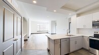 This 1,110-square-foot, third-floor apartment at 3411 Chestnut St in Philadelphia offers a well-designed single-level layout with 3 bedrooms, 2 bathrooms, 2 closets, and a combined kitchen and living area. The open-concept living room features large corner windows that flood the space with natural light and frame views of the surrounding Philadelphia cityscape, all complemented by wide-plank hardwood-style flooring and crisp white walls with blue-gray baseboards throughout. The modern kitchen is equipped with stainless steel appliances—including a French door refrigerator, range, and over-the-range microwave—white shaker cabinetry, white subway tile backsplash, and a peninsula with white quartz countertops. The primary bedroom spans 170 square feet, includes a ceiling fan, and connects directly to an en-suite bathroom featuring a dual-sink vanity with gray cabinetry, a glass-enclosed shower, and large-format tile flooring. A second full bathroom offers a single vanity and a glass-enclosed shower stall with tile surround. The unit also includes a spacious walk-in closet with wire shelving. Additional bedrooms are bright and versatile, each with hardwood-style flooring and ample wall space.