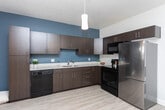 Located at 381 W Paxton Ave in Salt Lake City, Utah, this one-bedroom, one-bathroom unit offers a thoughtfully designed layout across a single floor. The kitchen is a standout feature, showcasing dark walnut-toned cabinetry, white countertops, and a bold slate-blue accent wall that adds a contemporary flair. It is fully equipped with stainless steel refrigerator, black electric range, built-in microwave, dishwasher, and a double sink — all illuminated by a stylish pendant light overhead. Light wood-style flooring runs throughout the main living areas, lending a clean, cohesive aesthetic. The living area continues the blue accent wall theme, creating a warm and modern atmosphere. A glass door opens to a private balcony, while a large window with blinds fills the space with natural light and outdoor views. The bedroom features plush carpeting, a window with blinds for natural light, and a quiet, restful ambiance. The bathroom is finished with wood-look flooring, a dark vanity with a white basin, and a full tub-shower combination. The textured ceiling and neutral tones throughout the unit provide a balanced, comfortable living environment ideal for urban living in Salt Lake City.