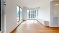 Located near the Gardiner Expressway in downtown Toronto, this one-bedroom, one-bathroom unit offers a well-designed layout across a single floor. Light hardwood flooring runs throughout, lending warmth and continuity to the clean, modern interior defined by crisp white walls and a minimalist aesthetic.

The living area is a standout feature, bathed in natural light through expansive floor-to-ceiling windows that frame impressive views of Toronto's urban skyline and surrounding cityscape. A built-in low-profile white storage unit runs along one wall, providing functional storage without disrupting the open feel of the space. The bedroom is comfortably proportioned, featuring its own large window with city views, a sliding door closet, and the same warm hardwood flooring found throughout the unit.

The bathroom is finished with large-format beige tiles, a wood-toned vanity with an integrated white countertop, and clean, understated fixtures that complement the home's contemporary design. A practical in-unit stacked washer and dryer is tucked neatly into a dedicated closet off the hallway, adding everyday convenience. The entrance and hallway connect all areas of the unit efficiently, making the most of the compact yet functional floor plan. Recessed lighting throughout enhances the bright, airy atmosphere of this city-view residence.