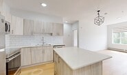 This thoughtfully designed two-bedroom, two-bathroom unit at 9660 229 St NW offers a well-utilized single-floor layout finished with contemporary materials throughout. Light hardwood flooring runs continuously across all rooms, creating a cohesive and bright interior.

The kitchen serves as a central feature of the unit, equipped with light wood-grain cabinetry, white subway tile backsplash, stainless steel appliances including a refrigerator, stove, microwave, and dishwasher, and a quartz-topped island that provides additional workspace and casual dining potential. A geometric pendant light adds a modern accent above the island.

The living area is open to the kitchen and benefits from recessed lighting. Both bedrooms are bright and well-proportioned, each featuring large windows with roller blinds that bring in natural light and outdoor views, along with baseboard heating units. The primary bedroom offers a comfortable footprint suitable for a full bedroom suite.

Both bathrooms are consistently finished with warm wood-tone vanities, white quartz countertops, undermount sinks, and full tub-shower combinations. A dedicated laundry area houses a stacked washer and dryer unit, adding everyday convenience within the home.