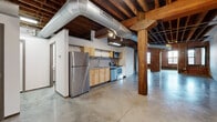 Located at 2017 Washington Ave in St. Louis, Missouri, this single-floor industrial loft space showcases a compelling blend of historic character and modern utility. The open-plan layout is defined by exposed red brick walls, original heavy timber structural columns, and warm wood-planked ceilings supported by raw timber beams. Polished concrete floors run throughout, lending a cohesive industrial aesthetic across the entire space.

Large, arched and rectangular black-framed windows punctuate the brick walls, drawing in abundant natural light and offering views of the surrounding St. Louis streetscape. Oversized silver ductwork runs visibly along the ceiling, reinforcing the raw, warehouse-inspired design.

The kitchen area is equipped with stainless steel appliances—including a refrigerator, range, microwave, and dishwasher—set against light wood cabinetry. A movable partition wall provides flexible space division within the expansive main area, which also features sections with clean white-painted walls ideal for display or presentation purposes.

The bathroom includes a shower/tub combination and a separate water closet. A corridor connects the functional areas, with original timber posts adding to the historic industrial ambiance throughout. This space is well-suited for creative, commercial, or live-work uses.