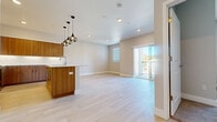 This single-floor residence showcases a thoughtfully designed open-concept layout, seamlessly connecting the living area and kitchen into one cohesive, light-filled space. Light-toned luxury vinyl plank flooring runs throughout the main living areas, complemented by neutral beige walls and clean white baseboards, creating a bright and contemporary atmosphere. A sliding glass door leads to a private balcony, allowing natural light to pour into the living space and providing outdoor views.

The kitchen is well-appointed with flat-front wood-grain cabinetry in a warm walnut tone, white quartz countertops, and a full suite of stainless steel appliances, including a range, microwave, and refrigerator. Under-cabinet lighting adds a polished, functional touch. A peninsula with a sink extends into the living area and is accented by stylish brushed-metal pendant lights, reinforcing the modern aesthetic.

The bedrooms offer plush carpeted flooring and window blinds for natural light control. One bedroom features direct balcony access via a sliding glass door. The full bathroom includes a tub-shower combination, wood-grain vanity cabinetry, white quartz countertop, and light tile flooring, maintaining the consistent design language found throughout the unit.