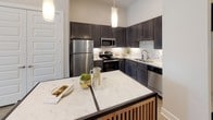 This single-story residence at 2865 Ridge Rd in Rockwall, Texas, offers a thoughtfully designed open layout with elevated ceilings throughout, contributing to a bright and airy atmosphere. Polished concrete floors run through the main living areas and bathrooms, providing a sleek, contemporary foundation that unifies the space.

The kitchen is a functional highlight, featuring dark espresso cabinetry extending to the upper walls, light granite countertops, a mosaic tile backsplash, stainless steel appliances, and a central island with additional counter space—ideal for both meal preparation and casual dining. Pendant lighting above the island adds a refined touch.

The living area is generously proportioned, with tall ceilings, large framed artwork, and direct access to an outdoor area through a glass-paneled door, allowing natural light to fill the room. Multiple bedrooms are present, each equipped with ceiling fans, ample natural light from well-placed windows, and walk-in closet access. Neutral tones and high ceilings give each room a calm, spacious character.

The bathrooms feature dark vanity cabinetry with granite countertops, large mirrors, and tub-shower combinations. Overall, the space presents a modern, cohesive aesthetic with quality finishes throughout.