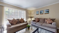 This single-floor residence offers a thoughtfully designed layout that balances comfort and functionality throughout its living spaces. The living room serves as the heart of the home, featuring wood-look tile flooring, elegant crown molding, and a large window dressed with vertical blinds that fills the room with natural light. Two plush sofas anchor the seating area around a glass-top coffee table, while a wall-mounted flat-screen TV and decorative artwork complete the space.

Adjacent to the living area is a charming dining room with crown molding, a pendant light fixture, and a built-in shelving unit framed by an arched opening — ideal for displaying décor or books. Linen drapes add a soft, casual elegance to the space.

The galley-style kitchen is efficiently designed with white cabinetry, granite-style countertops, and stainless steel appliances including a gas range and refrigerator, providing ample storage and workspace for everyday cooking.

The bedroom is a serene retreat, appointed with a ceiling fan, vertical blinds for light control, closet access, and warm neutral tones. The wood-look tile flooring flows consistently throughout, tying all rooms together with a cohesive, modern aesthetic. The overall ambiance is inviting, clean, and move-in ready.
