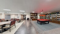 Located at 511 College Dr in Henderson, Nevada, this single-story community amenity facility offers a well-appointed and thoughtfully organized space designed to serve residents across multiple functional areas. The main common area is a bright, open dining and lounge space finished with large-format tile flooring and illuminated by recessed and flush-mounted ceiling lights. Multiple round tables with cushioned chairs are arranged throughout, fostering a social atmosphere. Large windows and glass doors along one wall invite natural light and provide direct views of an outdoor pool area, seamlessly connecting the interior to the exterior. A full kitchen with dark wood cabinetry, a bold orange accent wall, and a central island provides a communal food preparation and service area. A vending machine station and branded entry mat mark the main entrance. The recreation room features a classic billiard table beneath warm pendant lighting, surrounded by floor-to-ceiling bookshelves stocked with books and games, creating a cozy library-lounge ambiance. The dedicated exercise room is equipped with a comprehensive array of cardio and strength training machines, rubber flooring, ceiling fans, a large wall mirror, and motivational fitness-themed wall art, making it a fully functional workout facility. Together, these spaces offer a diverse and engaging environment for community living.
