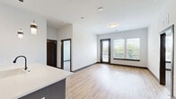 This well-designed 2-bedroom, 3-bathroom residence offers a thoughtful single-floor layout with contemporary finishes throughout. The open-concept kitchen and living area serves as the heart of the home, where light hardwood flooring flows seamlessly underfoot. The kitchen is outfitted with white upper cabinetry, stainless steel appliances including a French door refrigerator, microwave, and range, all complemented by a large central island featuring a quartz countertop, undermount sink, and a slate-blue base. Pendant lighting accents the space above the island, adding a modern touch. The living area extends toward a glass door with flanking windows, allowing abundant natural light and outdoor views to fill the room. The primary bedroom is a comfortable retreat with plush carpeting, a ceiling fan, and windows overlooking greenery. It connects to a private bathroom featuring granite countertops, gray cabinetry with matte black hardware, and a tiled tub-shower combination, plus a walk-in closet with wire shelving. The second bedroom also features carpet and a natural light source. Both closets offer organized wire shelving systems. Dark-trimmed interior doors and consistent hardwood-style flooring throughout the main areas provide a cohesive, polished aesthetic.