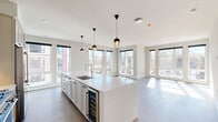 This well-appointed 2-bedroom, 2-bathroom residence offers a thoughtfully designed single-floor layout filled with natural light. The open-concept kitchen and living area serves as the heart of the home, anchored by a generous white quartz waterfall island with an integrated sink, built-in wine cooler, and stylish pendant lighting. The kitchen features sage-toned shaker cabinetry, stainless steel appliances including a gas range and French door refrigerator, and a clean white tile backsplash. Expansive floor-to-ceiling windows wrap the living area, flooding the space with sunlight and offering views of the surrounding neighborhood. Wide-plank hardwood flooring extends throughout the main living areas, complementing the neutral, contemporary palette. A private balcony is accessible from the living room. Both bedrooms are generously proportioned, each with plush carpeting and ceiling fans. The primary bedroom includes a walk-in closet with built-in shelving and direct access to an en-suite bathroom. The bathrooms are finished with marble-look tile, white quartz vanities, and shaker-style cabinetry. A clean, bright hallway connects the private quarters, and two well-organized closets provide ample storage throughout this modern, move-in-ready residence.