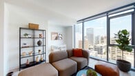 This contemporary high-rise unit offers a well-designed single-floor layout that blends modern aesthetics with functional living. The living area is the centerpiece of the space, anchored by expansive floor-to-ceiling windows that frame striking panoramic views of the surrounding urban skyline, flooding the room with abundant natural light. Light-toned wood-style flooring runs throughout, complementing the clean, neutral palette of the interiors.

A frosted glass sliding partition elegantly separates the living area from the sleeping quarters, offering privacy while maintaining an open, airy feel. The bedroom is appointed with a ceiling fan, a generous built-in closet, and warm, intimate lighting. The kitchen is outfitted with dark wood cabinetry, white countertops, and a full suite of stainless steel appliances, including a refrigerator, dishwasher, range, and microwave. A light-filled bathroom features wood-style flooring, a large vanity with ample cabinet storage, and a wide mirror with sleek matte black fixtures. A dedicated entryway with in-unit stacked washer and dryer adds everyday convenience. Throughout the space, the design balances modern minimalism with warm, livable touches.