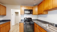This single-floor residence offers a thoughtfully laid-out interior with a clean, neutral palette that creates a bright and welcoming atmosphere throughout. The kitchen is well-equipped with warm honey-toned wood cabinetry extending to the ceiling for generous storage, dark granite-style countertops, a stainless steel sink, and black GE appliances including a gas range and over-the-range microwave. Light wood-look flooring runs through the main living areas, adding warmth and easy maintenance. A dedicated dining area features a chandelier and a sliding glass door with vertical blinds, allowing natural light to filter in and providing access to the outdoors. The living spaces are open and versatile, with crisp white walls and a clean, move-in-ready feel. The bedrooms are carpeted for comfort, each offering closet storage — one with a built-in shelving unit for added organization, and another with a standard reach-in closet. The bathroom includes a full soaking tub and shower enclosure finished with classic white subway tile, complemented by chrome fixtures and a medicine cabinet mirror. Throughout the residence, light-toned flooring, neutral walls, and consistent finishes create a cohesive and functional living environment.