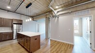 Located at 540 Broadway St in Saint Paul, MN, this four-bedroom, two-bathroom residence showcases a striking industrial-modern aesthetic across a single thoughtfully designed floor. Exposed concrete ceilings with visible ductwork and structural columns set a bold architectural tone throughout the open living areas, while light-toned hardwood-style flooring provides a warm contrast underfoot.

The kitchen is a standout feature, offering an expansive layout with rich dark wood cabinetry, bright white countertops, a large center island with pendant lighting, and a full suite of stainless steel appliances including a range, microwave, dishwasher, and refrigerator. The open-concept design connects the kitchen seamlessly to the living and dining areas.

Each of the four bedrooms features clean neutral walls and hardwood-style flooring, with select rooms offering large windows that frame views of the surrounding Saint Paul neighborhood, bringing in generous natural light. The industrial ceiling details carry through into the bedrooms, lending a cohesive urban character to the space.

Two full bathrooms serve the residence, one featuring a dual-sink vanity with dark wood cabinetry and white countertops. Two closets provide ample storage, including a walk-in closet with built-in wire shelving. The overall ambiance is contemporary and urban, blending raw industrial elements with modern, clean finishes.