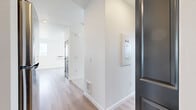 Located in Post Falls, Idaho, this thoughtfully designed unit offers a clean, modern aesthetic across a single floor. Light wood-style flooring flows seamlessly throughout the space, complementing the crisp white walls and creating a bright, cohesive atmosphere.

The living room is a standout feature, boasting tall ceilings and a wall of large black-framed windows paired with a glass-paneled door that opens to a balcony. This corner placement floods the room with natural light and frames sweeping views of the surrounding landscape, including distant mountains and open skies.

The kitchen is well-appointed with rich, dark-toned cabinetry, light countertops, and a full suite of stainless steel appliances including a refrigerator, electric range, microwave, and dishwasher. A built-in range hood adds a polished, functional touch, while the galley-style layout maximizes efficiency.

The bathroom is clean and minimalist, featuring a tub-shower combination, a natural light-admitting window, and chrome fixtures against all-white surroundings.

A dedicated in-unit laundry area includes a full-size top-load washer and dryer, providing added everyday convenience. The entryway, featuring a dark-toned front door and utility panel, leads smoothly into the main living spaces, making this unit as practical as it is visually appealing.