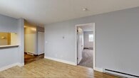 Located at 1201 Faichney Dr in Watertown, New York, this single-floor unit offers a well-organized layout with distinct living, dining, kitchen, and sleeping areas. The living room features warm hardwood-style flooring, soft gray walls, and a set of French doors fitted with blinds that invite natural light and provide outdoor access. Baseboard heating runs throughout the unit, ensuring year-round comfort. The dining area is defined by a elegant chandelier overhead and connects seamlessly to the kitchen via a pass-through counter with a wide opening, creating an open and communicative flow between spaces. The kitchen is equipped with white cabinetry featuring wood trim accents, a white electric coil-top range, a refrigerator, a stainless steel sink, light countertops, and tile flooring. The bedroom is carpeted and features two windows that bring in natural light from multiple directions, along with a generously sized bi-fold closet offering ample storage. The bathroom includes a full tub-shower combination, a single vanity with a large mirror, and tile flooring with darker accent walls. A textured ceiling is present in select areas, and white panel doors are consistent throughout the unit, contributing to a clean, cohesive interior aesthetic.