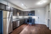 This single-story, one-bedroom, one-bathroom residence in Memphis, Tennessee offers a thoughtfully designed layout that balances functionality and comfort. The open living area is finished with warm hardwood-style flooring that extends throughout most of the unit, and large windows fitted with blinds allow natural light to fill the space while maintaining privacy. A ceiling fan with a light fixture adds both comfort and utility to the carpeted bedroom, which also benefits from multiple windows that bring in additional natural light.

The kitchen is a standout feature of the unit, equipped with an abundance of dark-toned wood cabinetry that extends to the ceiling for generous storage. Granite-style countertops provide ample workspace, and the stainless steel appliance suite includes an electric range, over-the-range microwave, dishwasher, and a double-basin sink. The kitchen's L-shaped configuration maximizes efficiency and flow.

The bathroom is clean and functional, featuring a soaking tub with a tiled surround, a curved shower rod, and an adjacent closet outfitted with wire shelving for organized storage. Neutral tones throughout the unit create a cohesive and inviting ambiance well-suited to a variety of furnishing styles.