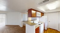 This single-story, one-bedroom, one-bathroom unit offers a practical and comfortable layout across a compact but efficiently utilized floor plan. The open-concept living and kitchen area serves as the heart of the home, where warm hardwood-style flooring flows through the kitchen while plush carpeting covers the spacious living room. A ceiling fan adds to the comfort of the living space, which is bathed in natural light through large windows and a sliding glass door that opens to an outdoor patio area.

The kitchen is thoughtfully designed with rich wood cabinetry, granite-style countertops, a peninsula breakfast bar, and white appliances including a range, microwave, refrigerator, and dishwasher. The galley-style layout maximizes counter and storage space efficiently.

The generously sized primary bedroom features neutral carpet flooring, clean white walls, and a closet, providing a quiet and functional retreat. The full bathroom is finished with wood-toned cabinetry, a white countertop vanity, a combined tub and shower unit, and hardwood-style flooring, maintaining a clean and cohesive aesthetic throughout.

Overall, the unit presents a bright, neutral palette with consistent warm wood accents, offering a move-in ready space suited for everyday living.