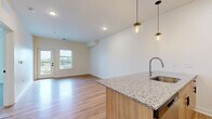 This thoughtfully designed one-bedroom, one-bathroom unit at 7510 N Oak Trafficway in Gladstone, Missouri offers a well-organized, efficient layout across a single floor. The open-concept living and kitchen area serves as the heart of the home, showcasing warm hardwood-style flooring, recessed lighting, and large windows and a glass door that allow generous natural light and provide access to an outdoor balcony with exterior views. The kitchen is a standout feature, complete with granite countertops, a peninsula island with an undermount sink, natural wood lower cabinetry paired with crisp white upper cabinets, stainless steel appliances including a refrigerator, range, microwave, and dishwasher, and stylish pendant lighting overhead. The living area is bright and open, flowing seamlessly from the kitchen. The spacious primary bedroom is carpeted for comfort, equipped with a ceiling fan, and benefits from two windows that bring in ample daylight. A closet provides dedicated storage. The bathroom features a full soaking tub and shower combination with built-in shelving, complemented by clean white finishes and hardwood-style flooring. A hallway connects the rooms with ease, completing this clean, modern, and move-in-ready layout.