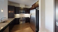 Located at 1620 E Jefferson St in Rockville, MD, this single-floor residence offers a well-appointed, modern living environment with thoughtfully selected finishes throughout. The kitchen is a standout feature, showcasing rich dark cabinetry that extends to the ceiling for ample storage, granite-style countertops, a classic tile backsplash, and a full suite of stainless steel appliances including a range, built-in microwave, and French door refrigerator. Durable wood-look flooring runs through the main living areas, lending warmth and a cohesive aesthetic. The open living area is bright and versatile, with clean white walls, recessed lighting, and a sliding glass door that opens to a private balcony overlooking the surrounding neighborhood and greenery, filling the space with natural light. The bedroom is generously sized, featuring plush neutral carpeting, warm taupe walls, and dual windows with views of the outdoors. The bathroom is finished with tile flooring, a dark-cabineted vanity with a white countertop, and a glass-enclosed walk-in shower with tile surround. Throughout the residence, clean architectural lines, neutral tones, and modern hardware create a polished, contemporary atmosphere suited to everyday living.