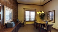 The business center at 825 E Palomar in Chula Vista is a single-floor workspace designed to blend functionality with warm, traditional aesthetics. The interior features rich, dark wood panel wainscoting that lines the walls, adding a polished and professional character to the room. Warm yellow-toned walls complement the wood detailing, creating an inviting yet productive atmosphere.

A built-in wood workstation runs along one wall, equipped with a computer terminal and printer, providing a practical setup for everyday business tasks. Plaid drape curtains frame a window fitted with blinds, allowing natural light to filter into the space while maintaining privacy. The window looks out to a landscaped exterior, adding a pleasant outdoor connection.

A round table with a stone-look surface is positioned near the window, accompanied by dark wood and upholstered chairs, offering a comfortable spot for meetings or collaborative work. Above the table, an elegant chandelier with warm-toned shades serves as a focal point, enhancing the room's refined, traditional ambiance. Neutral carpeting ties the space together, making it a well-appointed and welcoming business facility.