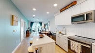 Located at 3850 Boston St in Baltimore's vibrant Canton neighborhood, this thoughtfully designed single-floor residence offers a seamless open-concept layout that connects the kitchen, dining, and living areas. The kitchen is outfitted with sleek white cabinetry, a herringbone tile backsplash, stainless steel appliances including a built-in microwave, range, and full-size refrigerator, and a large center island with a quartz countertop that provides additional seating. Light wood-tone flooring runs throughout the main living areas, enhancing the bright and airy atmosphere created by recessed lighting overhead. The living room is anchored by a sliding glass door that opens to a private balcony, allowing natural light to pour in and offering views of the surrounding community. Two well-appointed bedrooms feature plush carpeting, large windows with neighborhood views, and ample wall space. The bathroom is finished with light wood vanity cabinetry, a white quartz countertop, a large mirror, and clean tile flooring. Throughout the residence, a cohesive modern aesthetic is complemented by thoughtful design details, making this a comfortable and functional home in one of Baltimore's most sought-after urban communities.
