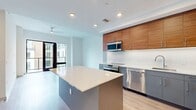 This contemporary 820 square foot apartment offers a harmonious blend of style and functionality. The open-concept living area is bathed in natural light, courtesy of large glass doors leading to a private balcony. Light wood-look flooring flows throughout, creating a sense of continuity and spaciousness.

The kitchen is a standout feature, boasting sleek gray cabinetry complemented by warm wood upper cabinets. Stainless steel appliances, including a French door refrigerator and built-in microwave, add a modern touch. A generous island with a white countertop provides additional prep space and casual dining options.

The bedroom, while compact at 90 square feet, offers a cozy retreat with ample natural light. Two closets in the apartment ensure sufficient storage space. The bathroom impresses with its glass-enclosed shower featuring trendy herringbone tile work, a floating wood vanity, and large-format floor tiles.

High ceilings and recessed lighting throughout enhance the apartment's airy feel. The thoughtful layout maximizes the use of space, making this one-bedroom unit feel much larger than its 820 square feet would suggest. Located at 101 N Meridian, this apartment offers modern urban living in a well-designed, efficient space.