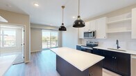 This thoughtfully designed one-bedroom, one-bathroom residence offers a functional and contemporary layout across a single floor. The open-concept kitchen is a standout feature, showcasing two-tone cabinetry with crisp white upper cabinets and bold navy lower cabinets, a subway tile backsplash, quartz countertops, and a full suite of stainless steel appliances including a refrigerator, range, microwave, and dishwasher. A center island with pendant lighting in matte black and gold adds both style and additional prep space. Light hardwood flooring flows throughout the main living areas, enhancing the bright, airy atmosphere. Sliding glass doors lead to a private balcony, bringing in natural light and outdoor views of the surrounding neighborhood. The bedroom is carpeted for comfort and features a large window with expansive views, plus access to a dedicated closet. The bathroom is finished with warm wood-tone flooring, a dark-cabinetry vanity with a mirror, and a full tub-shower combination. A stacked in-unit washer and dryer is also included. Clean lines, modern fixtures, and a cohesive neutral palette give this residence a polished, move-in-ready feel throughout.
