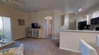 This single-floor, 2-bedroom, 2-bathroom residence is thoughtfully designed to maximize comfort and functionality. The open-concept living area features plush carpeting, neutral warm-toned walls, and crown molding that lends a polished, refined look throughout. Elegant arched doorways serve as architectural focal points, adding character and a sense of flow between spaces.

The living room is generously proportioned, providing ample room for furnishings and everyday living. It connects seamlessly to the kitchen area, which features a raised breakfast bar peninsula — ideal for casual dining or additional workspace. The kitchen is equipped with light-toned cabinetry and a functional layout designed for efficient use of space.

Crown molding detailing continues throughout the common areas, complementing the clean, neutral color palette that gives the home a bright and welcoming ambiance. Ceiling vents are integrated discreetly, ensuring consistent climate control. The arched hallway leads to the private bedroom and bathroom areas, offering a clear separation between living and sleeping quarters.

Overall, the residence presents a cohesive, comfortable interior with classic architectural detailing, practical design, and a neutral aesthetic that provides a versatile backdrop for a variety of décor styles.