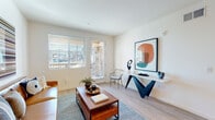 This single-floor residence in Brentwood, California offers a contemporary design defined by clean lines, crisp white walls, and light wood-style flooring that flows consistently throughout the space. The living area is bright and welcoming, benefiting from natural light through a large window and a glass-paneled door that opens to an outdoor area with views of the surrounding community. The room accommodates both a comfortable seating arrangement and a stylish console area, creating a versatile, functional layout.

The kitchen is thoughtfully designed with light wood cabinetry extending to the ceiling for ample storage, white quartz countertops, stainless steel appliances including a full-size refrigerator and range, and space for a central dining table, making it practical for both cooking and casual dining.

The primary bedroom is generously proportioned with a large window providing natural light and neighborhood views, while a second bedroom offers a quieter, cozier setting with its own window. Both rooms feature the same consistent light flooring.

Two bathrooms serve the residence — one with light wood cabinetry, a white countertop vanity, and wood-look flooring, and a second more spacious bathroom with a shower and clean, minimal finishes throughout. The overall ambiance is modern, neutral, and move-in ready.