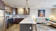 Located on Euclid Avenue in downtown Cleveland, this single-floor residence showcases a contemporary open-concept design that seamlessly integrates the kitchen and living areas. The kitchen is a standout feature, equipped with rich dark-walnut cabinetry — including glass-front upper cabinets — a mosaic tile backsplash in blue-grey tones, white quartz countertops, and stainless steel appliances. A large kitchen island with bar seating and stylish pendant lighting serves as both a functional workspace and a social gathering point. The adjoining living area benefits from large windows that invite natural light and offer urban views of the Cleveland streetscape.

The unit includes multiple bedrooms, each finished with wood-look flooring and neutral walls. One bedroom features a distinctive clerestory window near the ceiling, adding an architectural detail while maintaining privacy. A private hallway connects the bedrooms to two full bathrooms, each featuring a glass-enclosed walk-in shower, tile surround with mosaic accents, and dark-wood vanities with stone countertops. Wood-look flooring flows consistently throughout the unit, tying the spaces together with a cohesive, modern aesthetic suited to urban living.