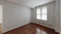 Located on Walnut Street in Philadelphia, PA, this single-floor unit offers a clean and functional layout designed for comfortable everyday living. The kitchen is well-appointed with white shaker-style cabinetry — both upper and lower — dark granite-look countertops, a stainless steel gas range, a stainless steel refrigerator, and an undermount sink. Neutral taupe tile backsplash accents the cooking area, while light tile flooring keeps the space bright and easy to maintain. The kitchen connects directly to the main living areas, allowing for an efficient flow throughout the unit. The living and bedroom spaces feature rich, dark hardwood floors that lend warmth and character to the neutral gray walls. Natural light filters in through windows fitted with horizontal blinds, and baseboard heating units are positioned beneath the windows throughout. Closet access is available in the bedroom areas via white paneled doors. The bathroom is finished with large-format gray marble-look wall tiles surrounding a full soaking tub with an overhead shower, complemented by chrome fixtures and a clean, modern aesthetic. Overall, the unit presents a straightforward, well-maintained interior with classic architectural details and practical finishes throughout.