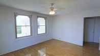 This single-floor space presents a clean, straightforward layout that emphasizes comfort and functionality. The interior is characterized by warm hardwood floors that run throughout, lending a timeless and inviting feel to the space. Neutral white walls provide a bright, airy backdrop that makes the room feel open and versatile.

Natural light is a standout feature, with two double-hung windows framed by classic white trim offering views of the surrounding neighborhood. The windows allow ample daylight to fill the space throughout the day, enhancing the sense of openness. A ceiling fan with an integrated light fixture is centrally mounted, providing both overhead illumination and air circulation for year-round comfort.

The room's simple, uncluttered design makes it highly adaptable for a variety of uses. Baseboards and clean wall finishes add a polished touch to the overall aesthetic. The well-maintained hardwood flooring reflects light beautifully, further contributing to the bright and welcoming atmosphere. Overall, this space offers a practical yet pleasant environment with classic architectural details and a neutral palette ready to accommodate a range of furnishing and décor styles.