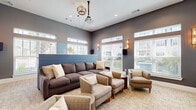 Located at 1110 Mason Pond Pl in Ladson, SC, this well-appointed screening and lounge room offers a sophisticated, multi-functional space designed for both entertainment and casual gathering. The room is finished in a contemporary palette of cool grays and crisp white trim, creating a polished and inviting atmosphere throughout.

At the heart of the space is a ceiling-mounted projector paired with a large wall-mounted projection screen, making it ideal for movie screenings or presentations. Built-in gray cabinetry with gold hardware runs the length of the wall beneath the screen, providing ample storage while adding a refined design touch. Recessed lighting and elegant wall sconces deliver warm, layered illumination.

The seating area features a large sectional sofa and an arrangement of upholstered armchairs centered around a textured area rug, offering comfortable viewing from multiple angles. A bar-height counter with striped stools lines one side of the room, functioning as a casual dining or social perch. Decorative artwork adds personality to the walls.

Multiple windows fitted with white horizontal blinds and transom windows above flood the room with natural light while offering views of the surrounding outdoor environment. The space is accessed through elegant frosted-glass French doors, completing its refined, community-lounge aesthetic.