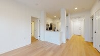 This single-floor residence features a clean, contemporary design defined by white walls, light hardwood-style flooring, and recessed lighting throughout. The open-concept living area is anchored by a white-mantled fireplace and flows seamlessly toward a set of French doors and windows that invite abundant natural light into the space.

The kitchen is thoughtfully designed with white shaker cabinetry accented by matte black hardware, a marble-style tile backsplash, white quartz countertops, and a full suite of stainless steel appliances including a refrigerator, range, microwave, and dishwasher. A peninsula with an integrated sink separates the kitchen from the main living area.

The bedrooms are well-proportioned, with ceiling fans and windows fitted with blinds. One bedroom connects directly to a generously sized en-suite bathroom featuring a dual-sink vanity with white quartz countertops, matte black fixtures, framed mirrors, and a glass-enclosed walk-in shower. A spacious walk-in closet with wire shelving provides ample storage.

Additional features include a dedicated in-unit laundry space equipped with a front-loading washer, and a hallway offering access to additional rooms. The overall ambiance is bright, clean, and move-in ready.