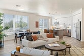 This well-appointed 2-bedroom, 2-bathroom residence offers a thoughtfully designed single-floor layout that balances style and functionality. Light-toned hardwood flooring flows throughout the main living areas, complemented by crisp white walls that enhance the sense of openness and brightness.

The open-concept living and dining area is a standout feature, bathed in natural light from large windows dressed with clean horizontal blinds. The living space comfortably accommodates seating and entertaining, while the adjacent dining area provides a dedicated space for shared meals with views of the surrounding greenery.

The modern kitchen is both stylish and practical, featuring white upper cabinetry, warm wood-toned lower cabinets, a quartz-topped island with bar seating, stainless steel appliances, and pendant lighting. A large window over the counter adds natural light to the workspace.

A welcoming hallway, accented with framed artwork, connects the living areas to the private bedrooms. Both bedrooms are carpeted and bathed in natural light, with the spacious primary bedroom offering a generous walk-in closet with dual hanging rods and shelving.

The bathrooms feature clean, contemporary finishes including wood-toned vanity cabinetry, white quartz countertops, large mirrors, and tile flooring. A balcony extends the living space outdoors, completing this well-rounded residence.