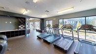 Located at 70 Upper Rock Circle in Rockville, Maryland, this comprehensive fitness center is designed to support a full range of workout routines in a modern, well-appointed environment. The space features durable rubber flooring throughout, smooth white ceilings with bright overhead lighting, and neutral gray walls that create a clean, focused atmosphere.

The cardio zone is equipped with multiple treadmills and Cybex elliptical machines, positioned along large windows that flood the area with natural light and offer views of the surrounding Upper Rock Circle development. A dedicated cycling alcove provides a more enclosed setting for stationary bike workouts.

The strength training area is outfitted with Hoist cable machines, plate-loaded equipment, and adjustable benches, complemented by a full rack of dumbbells displayed in front of wall-mounted mirrors that enhance the sense of space. A flat-screen television is mounted nearby for entertainment during workouts.

Structural columns are integrated throughout the floor plan, contributing to the architectural character of the space. Additional amenities include a wall-mounted equipment organizer and decorative shelving, adding both functionality and visual interest. The generous layout ensures ample room between stations, allowing for comfortable, unobstructed movement throughout the entire fitness facility.