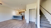 This thoughtfully designed two-story residence offers a bright and open layout that seamlessly connects the main living areas. The kitchen serves as a central focal point, featuring a striking blue island with a crisp white quartz countertop, stainless steel appliances including a refrigerator, range, and microwave, rich dark cabinetry, and stylish pendant lighting that adds a contemporary touch. The kitchen opens directly into a spacious living area finished with durable wood-look flooring, a ceiling fan, and large windows that invite abundant natural light and views of lush greenery outside. A convenient powder room on the main level includes a pedestal sink and mirror. The upper level is carpeted throughout and hosts a well-appointed hallway leading to multiple bedrooms. One bedroom features wood-look flooring, a ceiling fan, and a bright window with garden views, while another carpeted bedroom includes a wall-mounted mini-split unit and its own window overlooking the trees. A generously sized walk-in closet with wire shelving provides ample storage. The upper level also includes a full bathroom with a tub-shower combination. Clean white walls, consistent trim work, and an overall neutral palette give this residence a fresh, move-in-ready feel throughout.