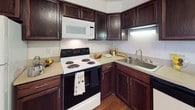 This single-floor residence offers a thoughtfully arranged layout that balances comfort and functionality. The kitchen is a standout feature, showcasing rich dark wood cabinetry that extends to the ceiling, light-toned countertops, and a full suite of appliances including a range, built-in microwave, and dishwasher. A peninsula with an undermount sink provides additional prep space and opens toward the dining and living areas, which are finished with warm hardwood-style flooring. The dining area is bathed in natural light thanks to a large sliding glass door framed by elegant window treatments, offering a pleasant view of the surrounding greenery outside. Two carpeted bedrooms provide comfortable retreats, each featuring neutral tones and ample closet storage. The primary bedroom includes a dedicated closet and an en-suite bathroom, while the second bedroom benefits from a bright window with outdoor views. Both bathrooms are finished consistently with dark wood vanities, light countertops, and classic fixtures. A secondary full bathroom with a tub-shower combination is conveniently accessible from the hallway. Throughout the space, neutral wall colors, carpet, and hardwood-style flooring create a cohesive and inviting ambiance.