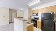 Located at 327 Guinevere Ln in Wilmington, NC, this well-appointed single-floor residence offers two bedrooms, two bathrooms, and a thoughtfully designed layout. The kitchen is equipped with warm oak cabinetry, black appliances including an electric range, built-in microwave, and refrigerator, anchored by a peninsula with a built-in sink and extended countertop that opens toward the living area. The living room is bright and airy, featuring plush carpeting, neutral walls, and a glass door that leads to an outdoor balcony, allowing ample natural light to fill the space. Both bedrooms are carpeted and feature ceiling fans, natural light from window blinds, and dedicated closets with wire shelving systems. The primary bedroom includes a generously sized walk-in closet. The bathrooms feature tile flooring, oak vanities with single-sink countertops, and a tub-shower combination. A dedicated laundry room with tile flooring includes washer/dryer hookups, wire shelving, and utility access. The overall aesthetic is clean and functional, with consistent neutral tones, white trim, and tile or carpet flooring throughout, offering a comfortable and practical living environment.